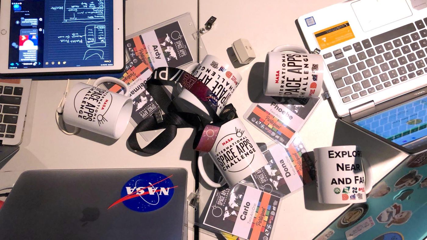 A desk with a laptop, notes and NASA mugs
